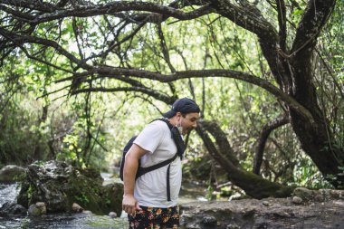 Siyah gömlekli ve siyah şapkalı bir adam nehir kıyısında yürüyor.