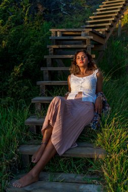 Elbiseli güzel bir kadın dağlarda bir bankta oturur ve kameraya bakar..