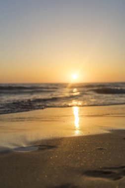 Sahilde güzel bir gün batımı, deniz dalgaları ve arka planda kum..