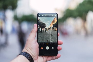 Barselona şehrinde bir adamın elinde cep telefonu ve modern bir caddenin fotoğrafı var.