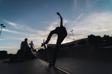 Gün batımının arka planında kaykaylı bir kadının silueti.