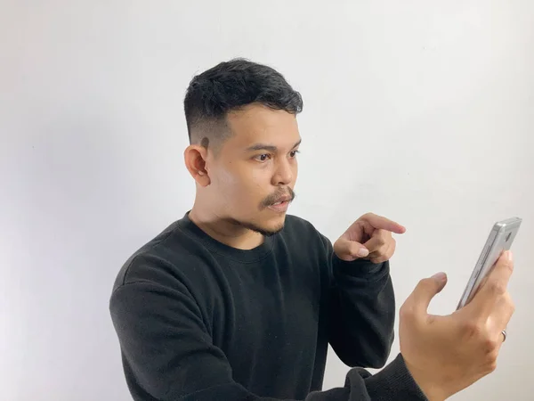 Молодий Азіатський Чоловік Показує Заплутане Обличчя Вказуючи Смартфон Ізольоване Сірому — стокове фото