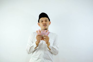 Asyalı Müslüman adam gülümserken beyaz arka planda kağıt para tutuyor.