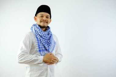 Siyah şapkalı Asyalı Müslüman adam kameraya gülümserken ayakta duruyor..