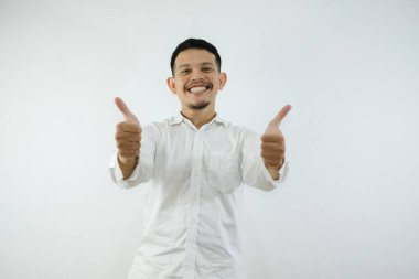 Beyaz arka plan üzerine sıradan gömlek giyen genç yakışıklı adam, olumlu bir jest yapıyor, gülümsüyor ve başarı için seviniyor. Kazanan jest.