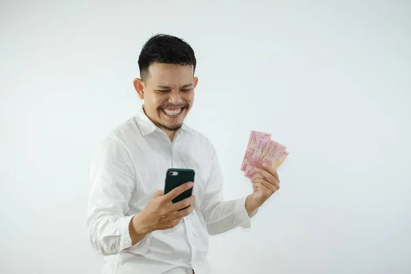 stock image Young adult Asian man holding money and showing happy expression when looking to his phone.