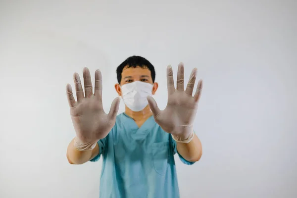 A young asian man wearing scrub suit and face mask showing stop hand gesture, close up of the hand.