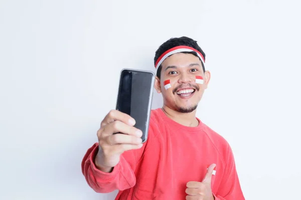 Stock image Indonesian man smiling while holding a mobile phone during independence day celebration