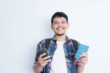 Endonezya pasaportu ve akıllı telefonu olan, kameraya gülümseyen genç bir Asyalı sırt çantalı. tatil ve seyahat kavramı