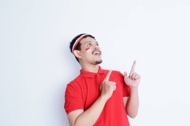 Genç Asyalı yetişkin, Endonezya 'nın bağımsızlık gününü kutlamak için iki eliyle beyaz arka planda bir şeyi işaret ediyor..