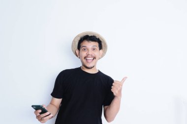 Asyalı bir adam cep telefonu tutarken gülümseyen siyah gömlekli ve plaj şapkalı.