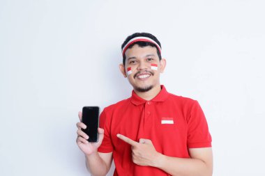 Saçbandı takan ve telefonunu gösteren gülümseyen Asyalı bir adamın portresi, beyaz arka planla izole edilmiş. Endonezya 'nın bağımsızlık günü konsepti