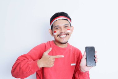 Saçbandı takan ve telefonunu gösteren gülümseyen Asyalı bir adamın portresi, beyaz arka planla izole edilmiş. Endonezya 'nın bağımsızlık günü konsepti