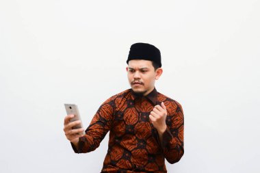 Suratında üzgün bir ifadeyle cep telefonu tutan Batik tişörtlü mutsuz Asyalı adamın portresi. Gri arkaplanda izole edilmiş resim