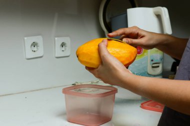 Bir kızın eli mutfakta mango soyuyor.