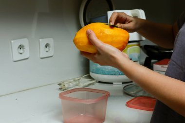 Bir kızın eli mutfakta mango soyuyor.