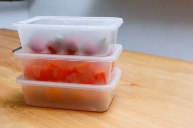 Tahta arka planda papaya, çilek ve portakal içeren plastik kaplar.