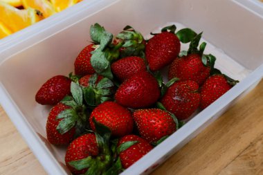 Tahta bir masada plastik bir kabın içinde çilekler.