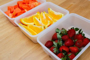 Tahta arka planda papaya, çilek ve portakal içeren plastik kaplar.