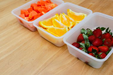 Tahta arka planda papaya, çilek ve portakal içeren plastik kaplar.