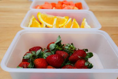 Tahta arka planda papaya, çilek ve portakal içeren plastik kaplar.