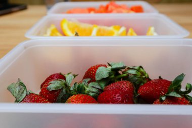 Tahta arka planda papaya, çilek ve portakal içeren plastik kaplar.