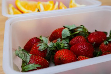 Tahta bir masada plastik bir kabın içinde çilekler.