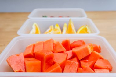 Tahta arka planda papaya, çilek ve portakal içeren plastik kaplar.