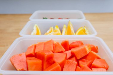 Tahta arka planda papaya, çilek ve portakal içeren plastik kaplar.