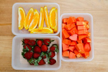 Tahta arka planda papaya, çilek ve portakal içeren plastik kaplar.