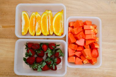 Tahta arka planda papaya, çilek ve portakal içeren plastik kaplar.