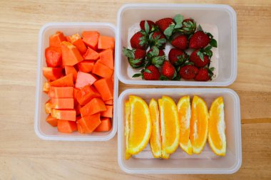 Tahta arka planda papaya, çilek ve portakal içeren plastik kaplar.