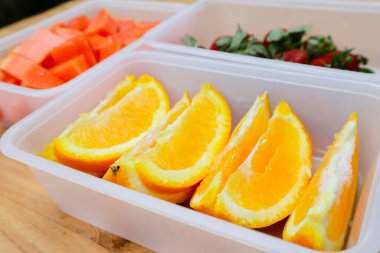 Tahta arka planda papaya, çilek ve portakal içeren plastik kaplar.
