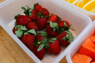 Tahta arka planda papaya, çilek ve portakal içeren plastik kaplar.