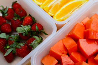 Tahta arka planda papaya, çilek ve portakal içeren plastik kaplar.