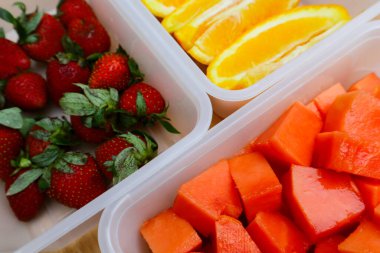 Tahta arka planda papaya, çilek ve portakal içeren plastik kaplar.