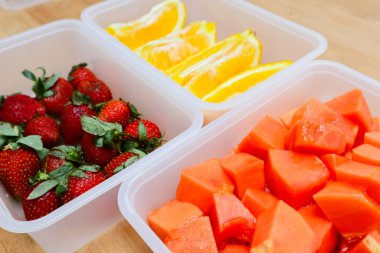 Tahta arka planda papaya, çilek ve portakal içeren plastik kaplar.