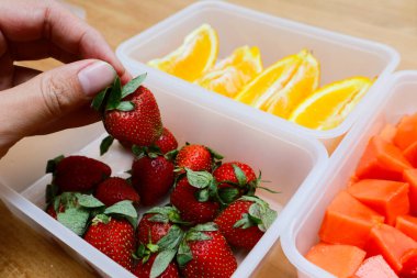 Tahta arka planda papaya, çilek ve portakal içeren plastik kaplar.