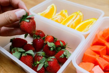 Tahta arka planda papaya, çilek ve portakal içeren plastik kaplar.