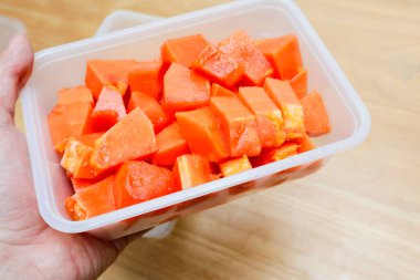 Tahta bir masada plastik bir kabın içinde küçük parçalara ayrılmış papaya meyvesi.