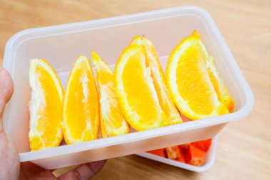 Tahta bir masada plastik bir kabın içinde sunkist portakal meyvesi.