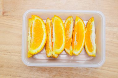 Tahta bir masada plastik bir kabın içinde sunkist portakal meyvesi.