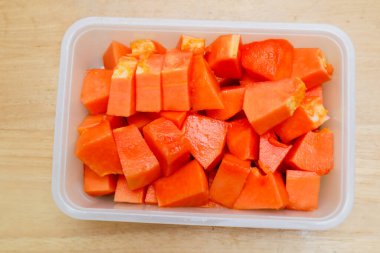 Tahta bir masada plastik bir kabın içinde küçük parçalara ayrılmış papaya meyvesi.