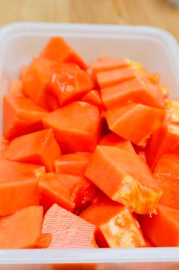 Tahta bir masada plastik bir kabın içinde küçük parçalara ayrılmış papaya meyvesi.