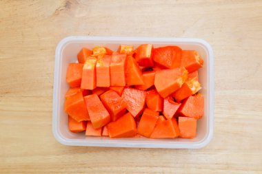 Tahta bir masada plastik bir kabın içinde küçük parçalara ayrılmış papaya meyvesi.