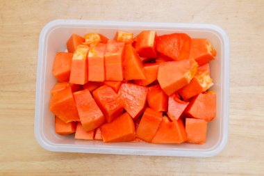 Tahta bir masada plastik bir kabın içinde küçük parçalara ayrılmış papaya meyvesi.