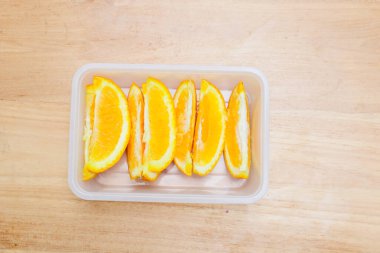 Tahta bir masada plastik bir kabın içinde sunkist portakal meyvesi.