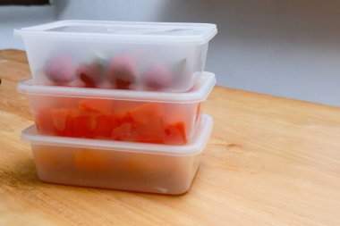 Tahta arka planda papaya, çilek ve portakal içeren plastik kaplar.