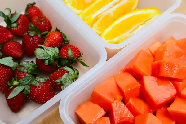 Tahta arka planda papaya, çilek ve portakal içeren plastik kaplar.