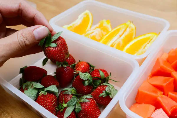 Tahta arka planda papaya, çilek ve portakal içeren plastik kaplar.